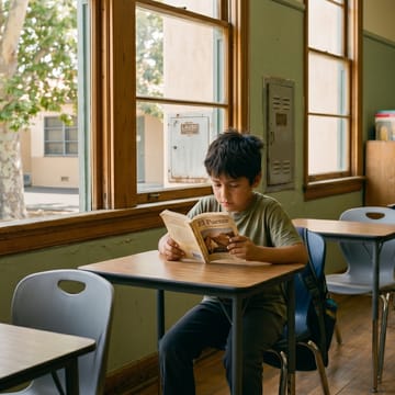 Twice-exceptional boy reading alone at a classroom desk surrounded by empty seats